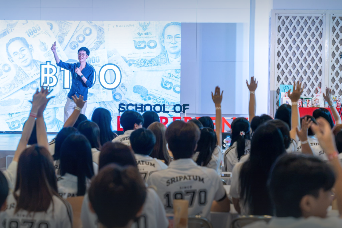 Phonlawat Sirajindapirom auctions a 100-baht note to the hall. Hands go up everywhere, but nobody bids above its value